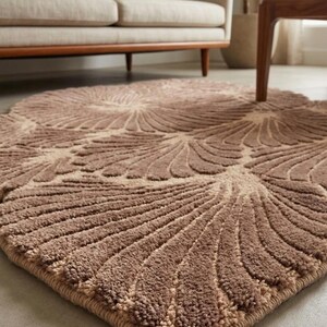 May include: A rectangular area rug featuring a repeating fan-like pattern in shades of brown and beige. The rug has a textured, tufted pile surface with a thick, stitched border edge that follows the contour of the repeating shell-like motifs.