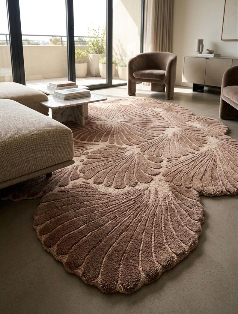 May include: A large, irregularly shaped area rug in a muted taupe color, featuring a repeating pattern of raised, fan-like shell motifs with deep grooves. The rug has a thick, textured pile and covers a significant portion of the floor space.