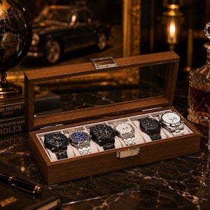 Peut inclure: Un coffret de rangement rectangulaire en bois pour montres, doté d'un couvercle en verre à charnière et d'un fermoir en métal argenté. L'intérieur comporte six compartiments individuels, chacun contenant une montre avec un bracelet à maillons.