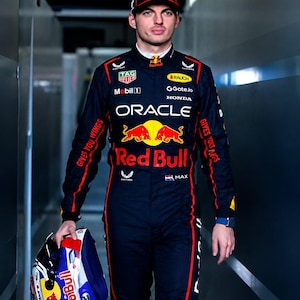 May include: A dark navy blue racing suit with red accents, featuring the Oracle Red Bull Racing logo, various sponsor patches, and the text Gives You Wings. A matching navy blue cap with the number 1 and a multi-coloured racing helmet are included.