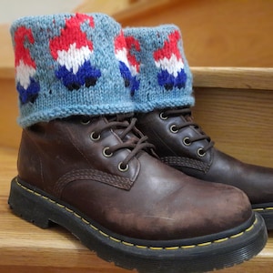 May include: Brown leather boots with black laces and a yellow stitch around the sole. The boots are worn and have a distressed look. The boots are topped with blue knitted leg warmers with a red, white, and blue gnome pattern.