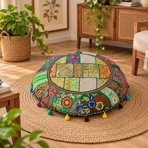 Peut inclure: Un coussin de sol rond présentant un motif patchwork vibrant avec divers panneaux de tissu verts, rouges et bleus. La surface est ornée de broderies complexes, de motifs floraux et d'accents de fils métalliques, finie avec de petits pompons colorés.