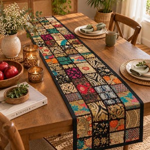 Peut inclure: Un long chemin de table rectangulaire composé d'un assemblage de carrés de tissu colorés aux motifs floraux et géométriques complexes dans des tons de rouge, d'or, de bleu et de noir, bordé d'un tissu noir uni.