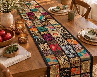 May include: A long rectangular table runner featuring a patchwork design of various colourful fabric squares with intricate floral and geometric patterns in shades of red, gold, blue, and black, finished with a solid black fabric border.
