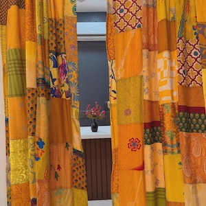 Pode incluir: Um par de cortinas de comprimento total com um design de patchwork composto por vários quadrados de tecido em tons de amarelo, laranja, verde e vermelho. Os painéis exibem uma mistura de padrões florais, geométricos e paisley, pendurados numa vara preta.