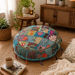 May include: A round floor cushion featuring a patchwork design of various fabrics in shades of teal, blue, red, and yellow. The cushion is decorated with intricate floral and geometric embroidery, finished with small colorful tassels along the edge.