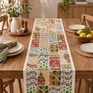Puede incluir: Un camino de mesa rectangular con un diseño de patchwork compuesto por varios cuadrados de tela. El camino muestra una mezcla de patrones que incluyen motivos florales, geométricos y abstractos en tonos verde, naranja, rojo y crema.