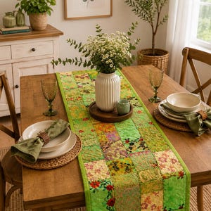 Pode incluir: Um caminho de mesa retangular com um design de patchwork de vários quadrados de tecido em tons de verde, amarelo e estampados florais. O caminho está sobre uma mesa de madeira, com um vaso branco canelado com flores brancas e folhagem.