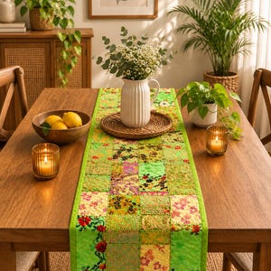 Peut inclure: Un chemin de table rectangulaire composé d'un patchwork de carrés de tissu aux motifs floraux et cachemire dans des tons verts, jaunes et roses. Il présente une bordure vert vif et des surpiqûres matelassées sur toute sa surface.