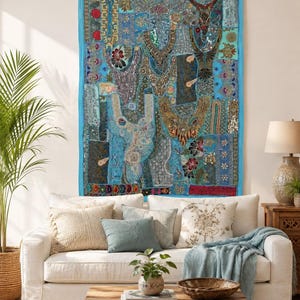 Könnte beinhalten: Ein rechteckiger Wandbehang mit einem lebendigen Patchwork aus blauen, türkisfarbenen und blaugrünen Stoffbahnen. Das Textil ist reich mit aufwendigen Stickereien, metallischen Pailletten, Perlen und Blumenmustern verziert und hat einen blauen Rand.