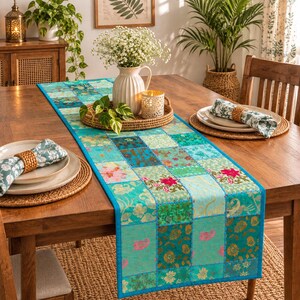 Könnte beinhalten: Ein rechteckiger Tischläufer mit einem Patchwork-Design aus verschiedenen Stoffquadraten in Türkis-, Blau- und Grüntönen mit Blumen- und Paisleymustern. Der Läufer liegt auf einem Holztisch mit weißen Tellern und passenden Servietten.