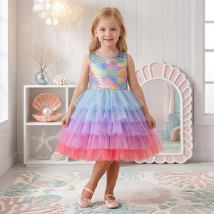 May include: A sleeveless dress featuring a shimmering, iridescent bodice with a quilted scale pattern. The skirt consists of multiple tiered layers of tulle in a gradient of light blue, purple, pink, and coral, ending at the knee.