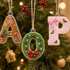 以下が含まれることがあります： 文字の形をした3つのクリスマスオーナメント（A、O、P）。Aは茶色のジンジャーブレッド風で、白いアイシング、雪の結晶、ヒイラギが描かれています。Oは赤いリボンが付いた緑色のリースです。Pは淡いピンク色で、白いアイシングとリボンで装飾されています。