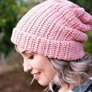 Puede incluir: Un gorro de punto de color rosa con un ajuste holgado. El gorro está hecho con un patrón de punto texturizado.