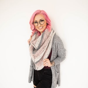 Puede incluir: Una mujer con el pelo rosa lleva una chaqueta de punto gris, pantalones vaqueros negros y una bufanda a rayas rosa, blanca y gris.