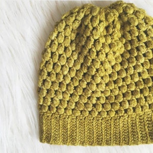 May include: A green crocheted beanie hat with a textured, bumpy design. The hat has a folded brim.