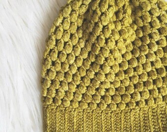 May include: A green crocheted beanie hat with a textured, bumpy design. The hat has a folded brim.