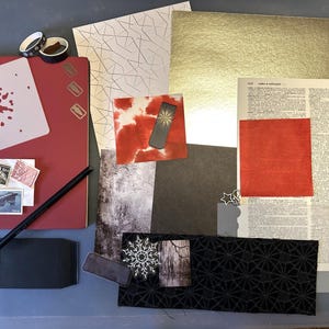 May include: A collection of craft supplies including a red notebook, a paint splatter stencil, vintage postage stamps, a black pencil, gold and patterned paper, a dictionary page, a red square, a black fabric strip with geometric patterns, and a snowflake.