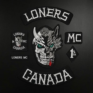 May include: A set of black and white embroidered patches featuring the text LONERS and CANADA in arched banners, a central skull-wolf hybrid graphic with green eyes and a red drop, a square patch with a skull, a rectangular MC patch, and a diamond 1%ER patch.