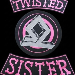 Peut inclure: Un ensemble de trois écussons brodés sur fond noir avec des fils roses et blancs. Les écussons incurvés en haut et en bas affichent le texte TWISTED et SISTER en rose. L'écusson circulaire central présente un logo géométrique blanc stylisé.