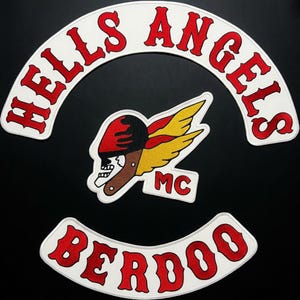 Puede incluir: Un conjunto de tres parches bordados que incluye un rocker superior arqueado blanco con texto rojo que dice HELLS ANGELS, un emblema central de calavera alada en rojo, amarillo y negro, y un rocker inferior blanco con texto rojo BERDOO y MC.