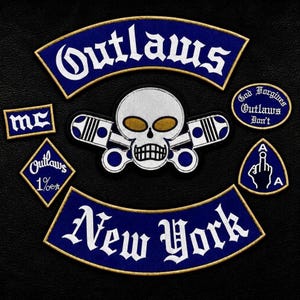 Könnte beinhalten: Ein Set aus gestickten Aufnähern mit einem zentralen Totenkopf mit goldenen Augen und gekreuzten Kolben, einem oberen Schriftzug Outlaws, einem unteren Schriftzug New York, einem MC-Aufnäher, einer 1%er-Raute, einem AFA-Schild und einem Oval.