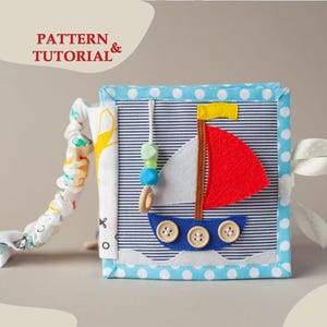 May include: A fabric activity book featuring the text PATTERN & TUTORIAL & on the cover. The cover displays a sailboat applique with a red sail, a blue hull with three wooden buttons, and a yellow flag. It has blue and white polka dot borders.