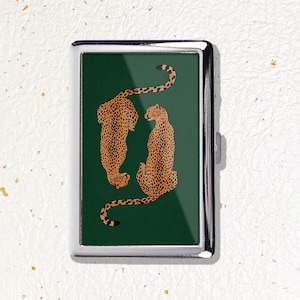May include: A rectangular metal case with a polished silver frame and a dark green insert. The insert features a graphic illustration of two spotted cheetahs in orange and black, positioned facing each other against the solid dark green background.