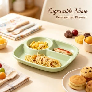 May include: A light green, three-section divided plate containing corn, spaghetti, and a piece of fish with red sauce. The text "Engravable Name" and "Personalized Phrases" appears in the upper right corner of the image.