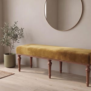 Puede incluir: Un banco rectangular con un asiento tapizado en terciopelo amarillo mostaza y una estructura de madera marrón oscuro con seis patas torneadas. El banco tiene una textura de superficie suave y afelpada y una base robusta con detalles tallados.