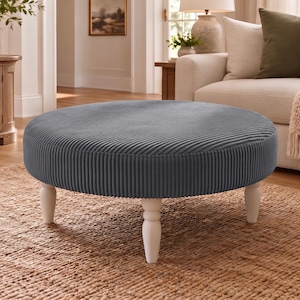 May include: A round ottoman upholstered in a dark blue corduroy fabric with a textured ribbed surface. The piece features four short, turned wooden legs finished in a matte white paint, providing a stable base for the circular cushioned seat.