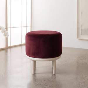 May include: A round ottoman featuring a deep burgundy velvet upholstered seat cushion. The base is constructed from light-toned wood and is supported by four short, tapered wooden legs that provide a stable foundation for the circular seat.