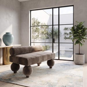 Peut inclure: Un banc en velours taupe doté d'un long dossier cylindrique et de quatre grands pieds sphériques. Le banc est recouvert d'un tissu doux et mat et est positionné près du sol, présentant un design géométrique épuré aux formes arrondies.