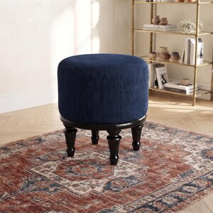 May include: A round, navy blue corduroy ottoman featuring a textured, vertically ribbed fabric surface. The piece is supported by four dark brown, turned wooden legs that provide a stable base for the circular, upholstered seat cushion.