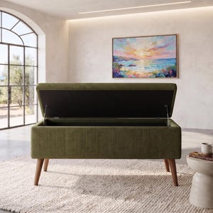 May include: An olive green corduroy storage bench with a rectangular hinged lid that is open. The bench features a textured fabric exterior and is supported by four tapered wooden legs. The interior of the lid is black and the base is rectangular.