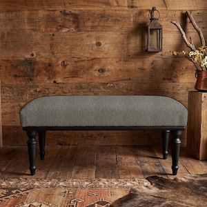 May include: A rectangular bench featuring a textured gray upholstered seat cushion supported by four black turned wooden legs. The bench has a clean, armless design with a smooth, rounded edge profile on the top seat surface and dark finish legs.