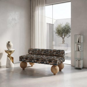 May include: A backless bench featuring a rectangular seat and a cylindrical bolster cushion, both upholstered in a multi-colored textured fabric with black, brown, and white patterns, supported by four large, spherical light-toned wooden legs.