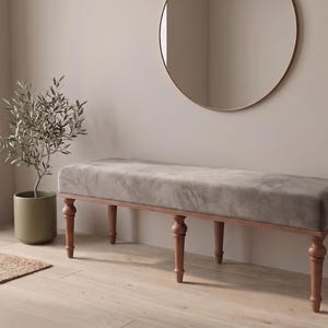 Puede incluir: Un banco rectangular con un cojín de asiento tapizado en gris, sostenido por seis patas de madera torneada en un acabado marrón cálido. El banco presenta un diseño largo y bajo con una textura suave y uniforme en toda la superficie.