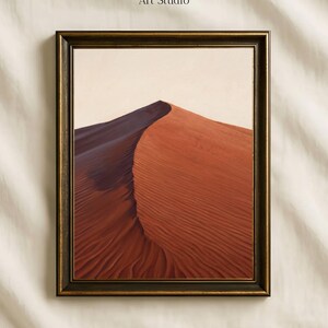 May include: A framed wall art print featuring a desert sand dune with a sharp contrast between deep red and dark purple shadows under a pale sky. The text Vintage Paper Art Studio is printed above the frame in a simple serif font.