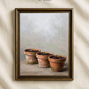 May include: A framed oil painting titled Vintage Paper Art Studio featuring three weathered terracotta pots arranged in a row, each containing a small green seedling, set against a soft, muted, and neutral-toned background with visible brushstrokes.