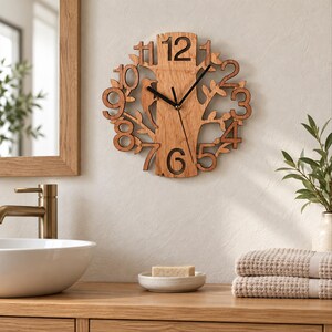 May include: A circular wooden wall clock featuring a tree trunk design with a carved bird silhouette. The clock face displays cutout numbers from one to twelve arranged around the central trunk, complemented by two thin black metal clock hands.