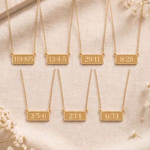 May include: Seven gold-toned necklaces, each featuring a rectangular pendant engraved with different numerical sequences: 119:105, 13:4-5, 29:11, 8:28, 3:5-6, 23:1, and 6:33. Each pendant is suspended from a delicate gold-toned chain link necklace.