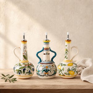 Può includere: Tre oliere in ceramica con disegni dipinti a mano. L'oliera a sinistra presenta rami d'ulivo, quella centrale ha intricati motivi floreali blu e arancioni con la parola OLIO, e quella a destra mostra limoni gialli e foglie verdi.