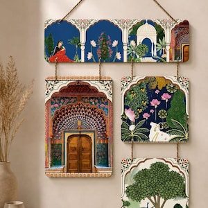 May include: A wall hanging set consisting of four rectangular panels suspended by ropes. The panels feature intricate illustrations of architectural arches, a person in a red garment, a white cow, a peacock, and lush green trees against blue backgrounds.