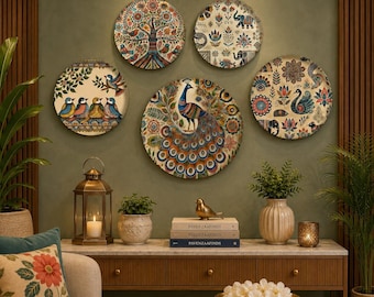May include: Five circular wall plates featuring intricate, colorful patterns including a tree of life, elephants, birds, and a central peacock. The plates are arranged on a wall above a wooden console table with a lantern, books, and plants.