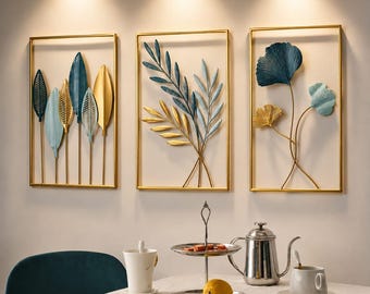 May include: Three rectangular wall art pieces featuring gold metal frames and botanical motifs. The designs include stylized leaves and ginkgo-like foliage in shades of navy blue, light blue, and gold. The text PAVENZAAFINDS is centered above.