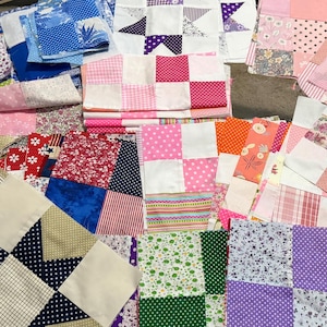 May include: A collection of assorted fabric quilt blocks featuring various patterns and colors, including pink, blue, purple, green, and white. The squares display floral, polka dot, plaid, and geometric prints arranged in patchwork designs.