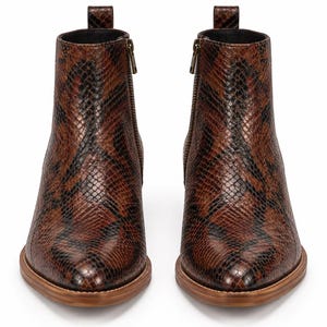 Puede incluir: Un par de botines con un patrón de piel de serpiente en marrón y negro. Los botines tienen punta afilada, cierre de cremallera lateral con tirador metálico y una lengüeta en la parte trasera. Las suelas son de un material color madera clara.