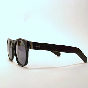 May include: Black sunglasses with a dark gray lens and a black frame. The frame has a silver logo that says "DXXO" on the right side.