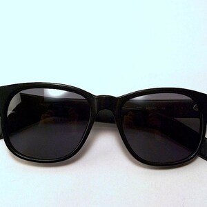 May include: Black plastic sunglasses with dark lenses. The sunglasses have a classic rectangular shape.